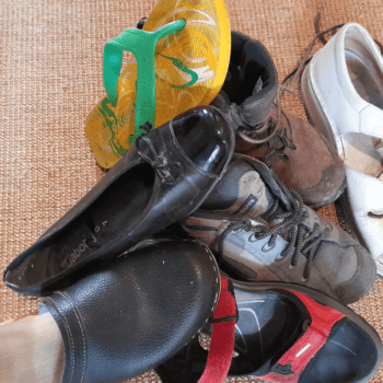 Unterschiedliche Schuhe (Schlappen, Ballerinas, Sandalen, Wanderschuhe, Flip Flops) sind auf einem Stapel zusammengewürfelt.